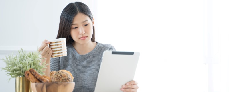 Imagen de Noticias en nuestra comunidad con una mujer sosteniendo una tableta y una taza de café.